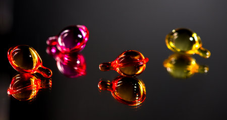 Colorful liquid-filled capsules, oil, serum, pink and yellow varieties, on black glossy, reflective surface. Capsules on grey background.の写真素材