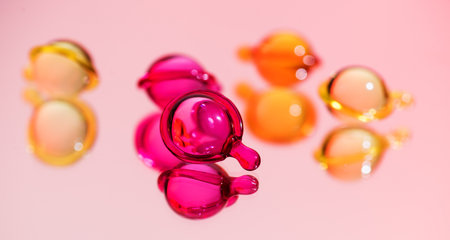 Cosmetic capsules, hair care oils, colorful liquid-filled capsules, oil, serum, pink and yellow varieties, glossy, reflective pink surface. Capsules background, vibrant, modern aesの写真素材