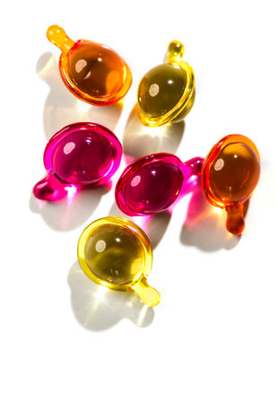 Cosmetic capsules for face or hair care, colorful liquid-filled capsules, oil, serum, pink and yellow varieties, glossy, reflective surface. Capsules background, vibrant, modern aeの写真素材