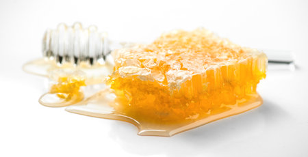 Fresh Honey in honeycombs dripping, pouring from a glass honey dipper spoon, on white background. Honeycomb close-up. Healthy organic liquid honey spillの写真素材