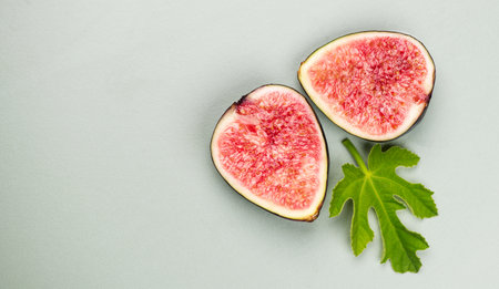 Fig fruits. Half of Ripe sweet fresh figs fruit with leaf close up, on pastel green background, flat lay, top view. Border art designの写真素材