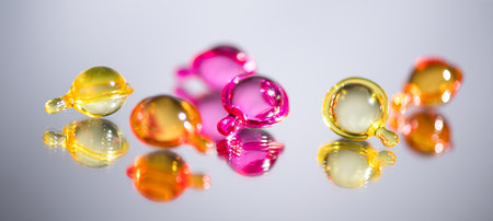 Cosmetic capsules for face or hair care, colorful liquid-filled capsules, oil, serum, pink and yellow varieties, glossy, reflective surface. Capsules background, vibrant, modern aeの写真素材