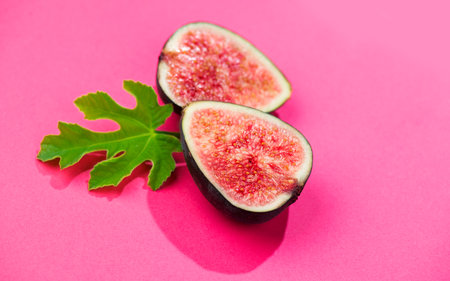 Fig fruits. Ripe sweet halved fresh figs fruit with leaf close-up, on pink background, flat lay, top viewの写真素材