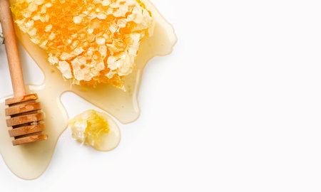 Honeycomb, honey dripping, pouring from wooden honey dipper spoon, isolated on white background, border design, close-up. Honey comb, Healthy organic liquid honey spill. Flat lay,の写真素材