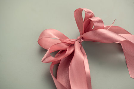 Pink satin gift bow over pastel background. Holiday decoration silk ribbon, top view, border art. Beautiful gift design.の写真素材