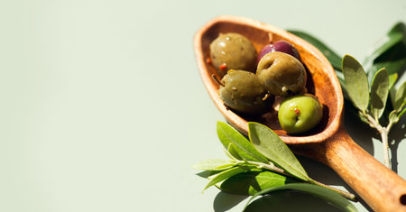 Olives, homemade marinated colorful olives with herbs and spices over green background, in a rustic wooden spoon, close up. Healthy Mediterranean vegan food. Border designの写真素材