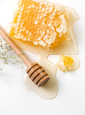 Honey in honeycombs dripping, pouring from wooden honey dipper spoon, on white background. Close-up. Healthy organic liquid honey spill, with flowers. Flat lay, top view, from abovの写真素材