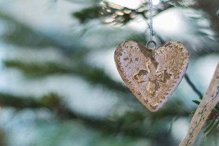 Designer Christmas card background with copy space, green xmas fir tree out of focus background with vintage white heart hanging decorationの写真素材