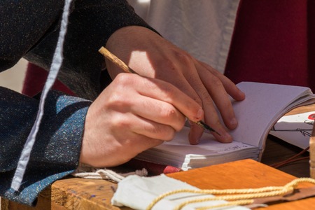 Close up of hands of scribe practicing traditional illumination writing calligraphy with feather quill and inkの写真素材