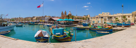 Traditional colourful Maltese Luzzu fishing boats in the turquoise blue water of Marsaxlokk harbour, with the beautiful Parish Church of Our Lady of Pompei, Marsaxlokk, Malta, June 2017のeditorial素材