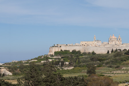 Ancient hilltop fortified capital city of Malta, The Silent City, Mdina or L-Imdina, skyline against blue Spring skies with huge walls, cathedral domes and towers, fields of spring flowersの写真素材