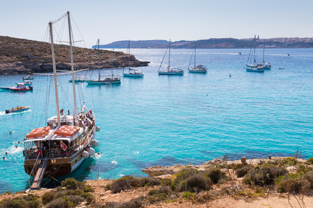 Yachts and boats bring tourists to the beautiful crystal clear azure turquoise blue waters of the Blue Lagoon on the small holiday island of Comino, Malta, June 2017のeditorial素材