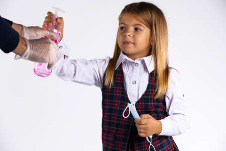 Confused little girl with medicinal mask in her hand and school uniform try to take the disinfectant in her handの写真素材
