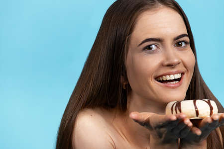 Pretty caucasian woman, wide smiling, hold a glaze white chocolate donut on her palms. Isolated over blue background.の写真素材