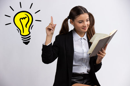 Beautiful teenage girl reading book and pointing up with finger on light bulb, isolated on white