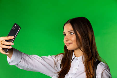Inspired trendy girl with long brown hair taking selfie. Cute brunette in white shirt posing on green backgroundvbvの写真素材