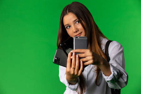 Attractive pretty woman in white shirt taking photo on two smartphones isolated on green background.の写真素材