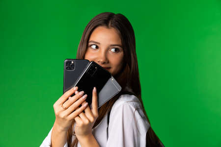 Teen schoolgirl with various smartphones. Content female teenager holding assorted modern mobile phones and looking away against green backgroundの写真素材