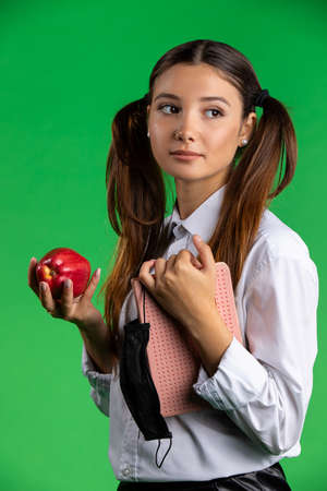 Teenage female student with apple and protective mask. Teen female student holding red apple and protective mask while standing against green backgroundの写真素材