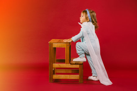 It looks magical. A little girl dressed in pajamas and wearing a white handmade superhero cloak,...