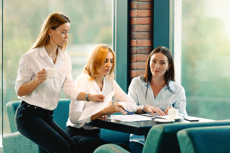 Group of three coworkers working together on business project in modern office. Young attractive caucasian woman smiling, teamwork concept. Horizontal, blurred background.の写真素材