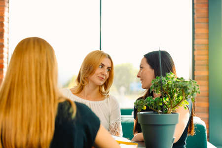 Girls gossip. Three best friends speaking in cafe. Smiling females friends falking and laughing while sitting at table in coffee shop. Social and friendship conceptの写真素材