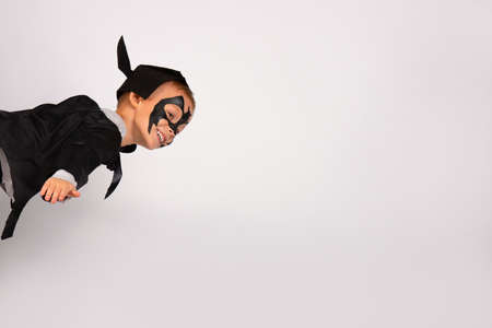 Happy superhero boy in black bat costume with hat and ears flying like lightning bolt in the sky. Portrait isolated on white background with plenty spaceの写真素材