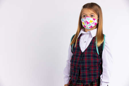 Portrait of primary schoolgirl with face mask going back to school.Covid-19 quarantine. Grey background with empty spaceの写真素材