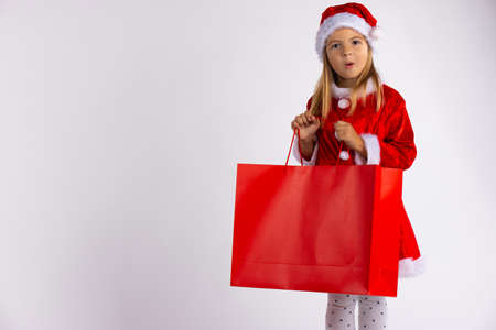 Exited little girl surprised by present found in the shopping bag. Kid on winter sale with gift, on white background .の写真素材
