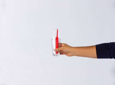 Photo of a set with red and white toothbrushes in a glass held in human hand on white background with plenty space, concept dental.の写真素材
