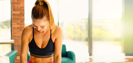 Young and slender fitness sport woman resting and posing embarrassedly during workout. Indoor shot with empty side spaceの写真素材