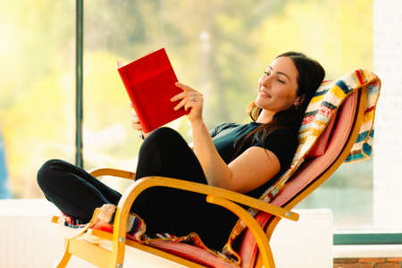 Young attractive woman reads a book swaying in a comfortable rocking chair. Having fun and having a good time improves your mood.の写真素材
