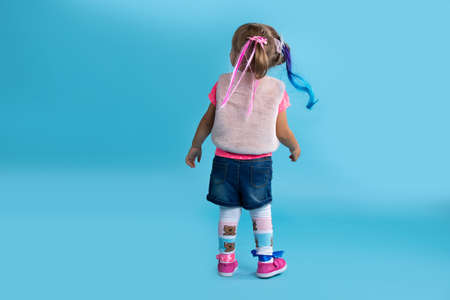 A little girl dressed in carnival costume turned to see something interesting behind. Photo on a blue background. Halloween concept. High quality photoの写真素材
