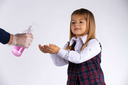 Caucasian schoolgirl disinfects her hands before entering the classroom isolated on white background. Virus and pandemic concept. High quality photoの写真素材