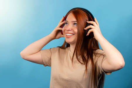 Beautiful young girl in headphones, listens to music, smiles and sings, isolated on a blue background with free space. High quality photoの写真素材