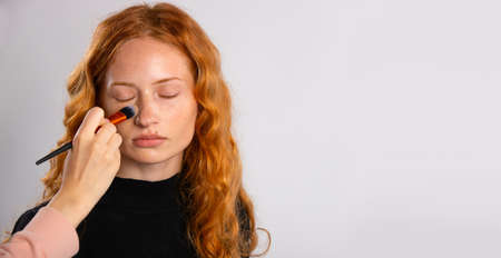 A young girl with red curly hair, with delicate makeup, which is powdered with a brush. Fashionable female model with beautiful appearance. High quality photoの写真素材