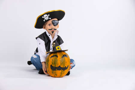 A boy with a serious face wearing a pirate hat. Nearby is a pumpkin in a black handmade hat. Both have rosy makeup. High quality photo on white background with blank space. High quality photoの写真素材