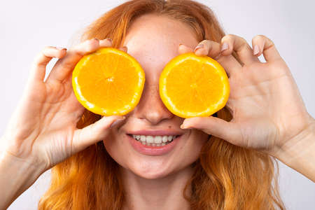 Beautiful redhaired joyful girl with freckles, red curls and yellow makeup. Orange slices and laughter, emotions. Beauty and spa concept. High quality photoの写真素材