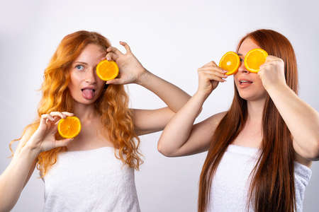 Red-haired girlfriends are having fun and posing with orange slices. Healthy food, spa and beauty, vitamins and happiness concept. Photo on white background. High quality photoの写真素材