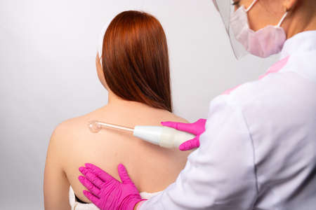 An cosmetologist apply darsonval gently rubbing it all over the back. Health and personal care concept. Photo on white background. High quality photoの写真素材