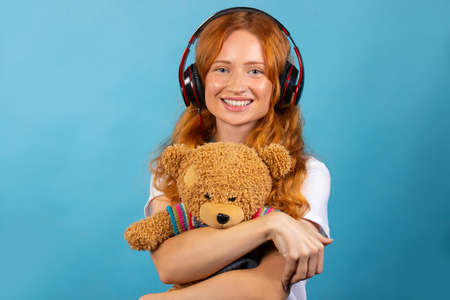 Girl with her beloved bear. Listens to music with headphones, posing and smiling. Photo on a blue background. High quality photoの写真素材