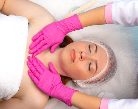 Close-up of a young woman receiving a cosmetic facial massage in a beauty salon and the hands of the master in pink gloves are visible. Facial care. Spa. High quality photoの写真素材