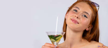 Banner, long format. Happy girl with sun glasses on her head and holding a cocktail in her hands. Isolated on white background. Summer and vacation concept. High quality photoの写真素材