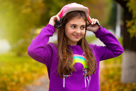 A girl with a happy smile puts on a hard-wearing helmet for cycling in an autumn park. Rest and time...