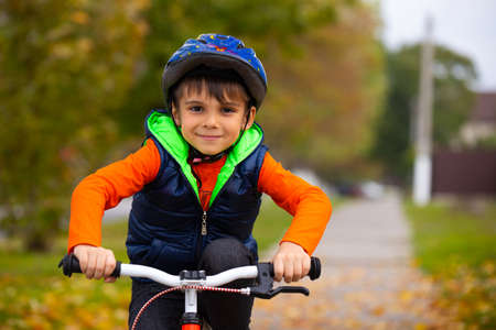 Boy in the autumn park. Small child wearing a helmet and riding a bicycle on an autumn day. Active healthy outdoor sports. High quality photoの写真素材