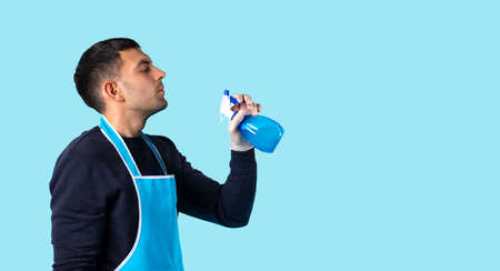 Banner, long format. A man with rubber gloves and a spray gun in his hands, sprays into the air. Photo on blue background with large empty side space. High quality photoの写真素材