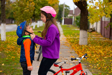 Safety comes first. The sister helps the younger brother to put on and fasten the protective helmet. The concept of safety, rest and spending time. Photo with empty side space. High quality photoの写真素材