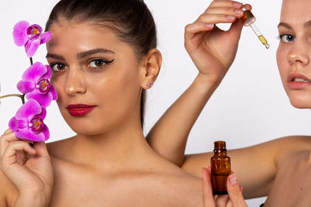 Beautiful cute girls advertise moisturizing serum on their face. In hands holding an orchid flower. Concept for skin care, regeneration, restoration.の写真素材