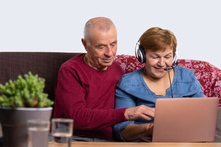 A woman works at home using a computer via video communication with a headset. The man became interested in her work. Senior online and pandemic concept.の写真素材