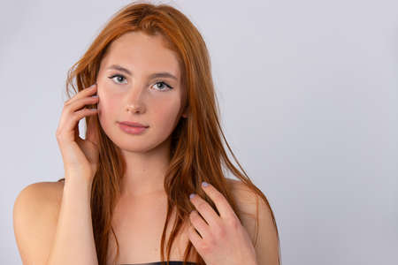 Red-haired girl with long and healthy hair. With clean, soft and healthy skin on a gray background. Photo with empty side space. Healthy hair and clean skin conceptの写真素材